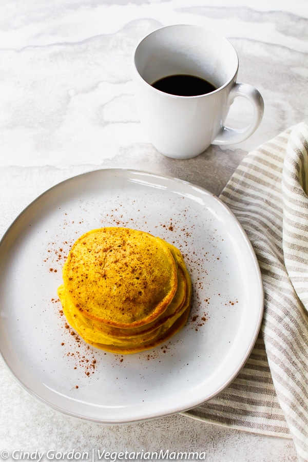a stack of Gluten Free Pumpkin Pancakes on a plate with a cup of coffee