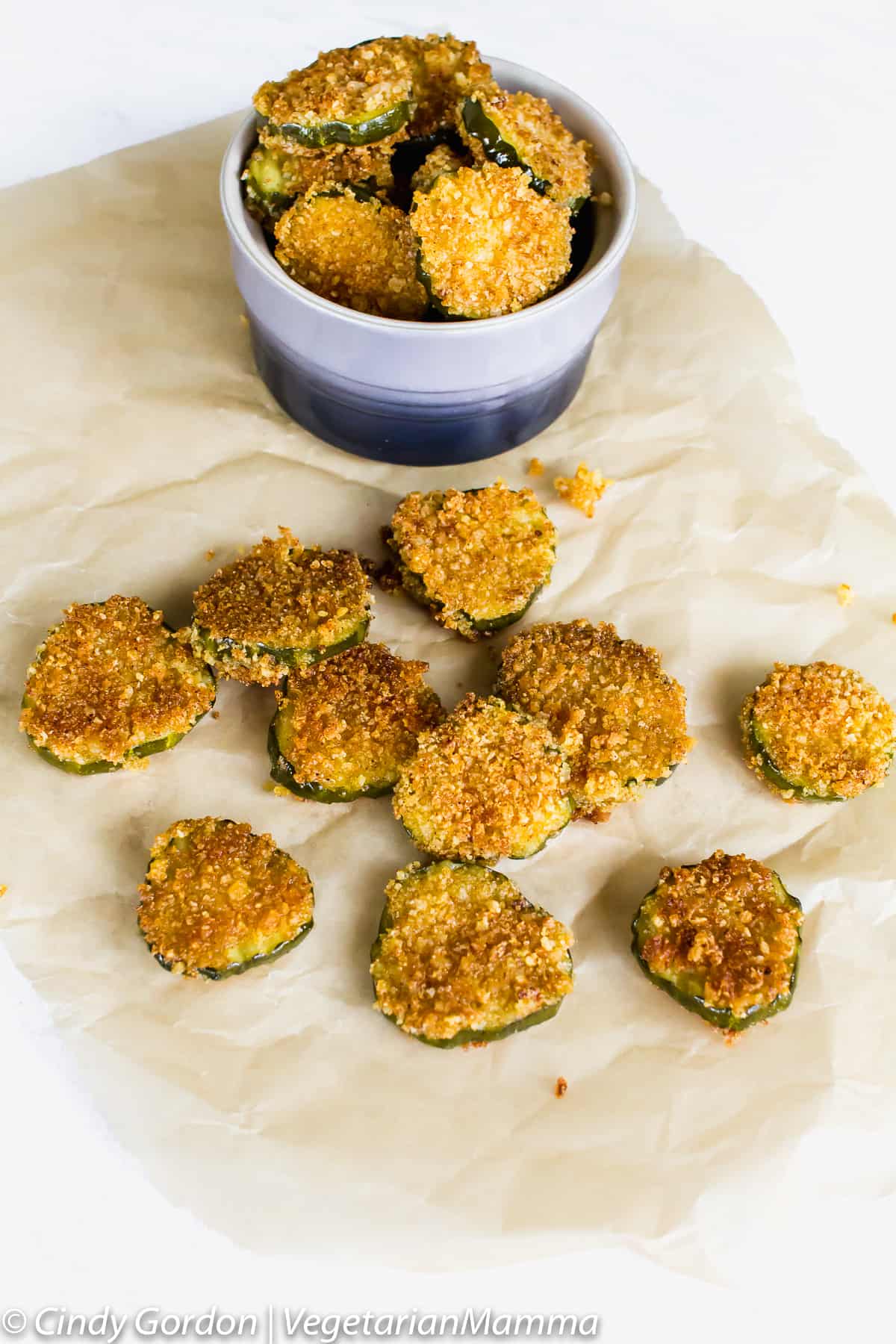 Gluten Free Fried Pickles in a cup on top of a piece of crumpled parchment paper. several pickles are outside of the cup on the paper as well. 