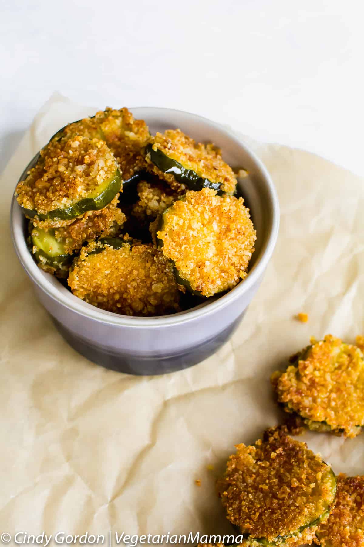 Gluten-Free Fried Pickles on a crumpled piece of parchment paper. some are on the paper, some are in a small bowl. 