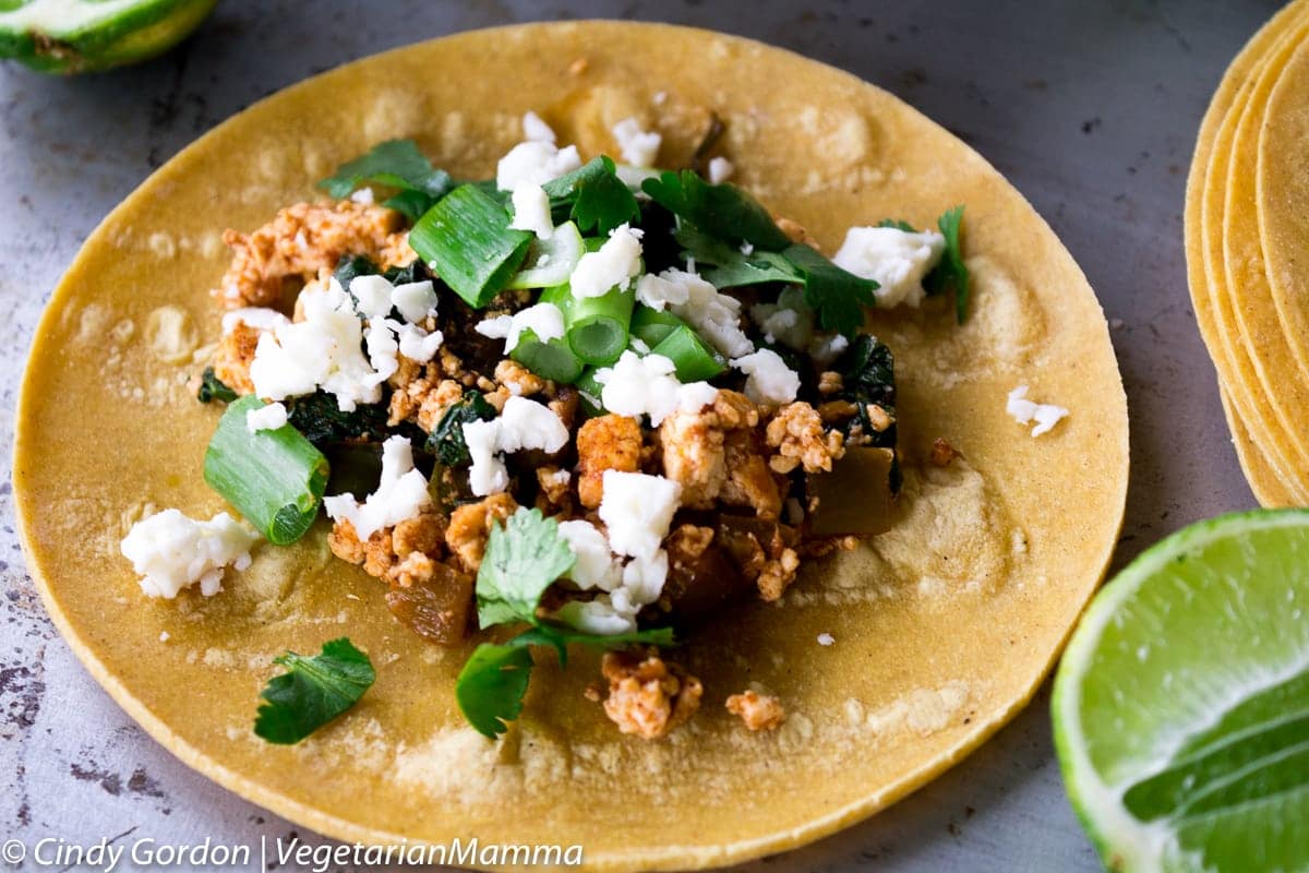 tofu scrambled with green vegetables and cilantro topped with crumbly white cheese on a corn tortilla