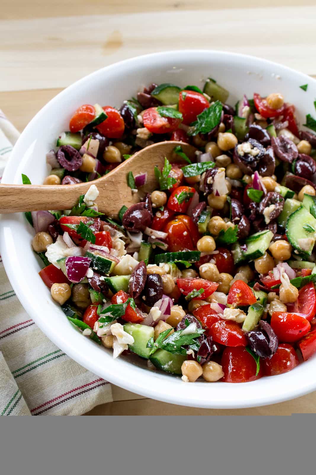 Mediterranean Chickpea Salad in white bowl with wooden spoon inside