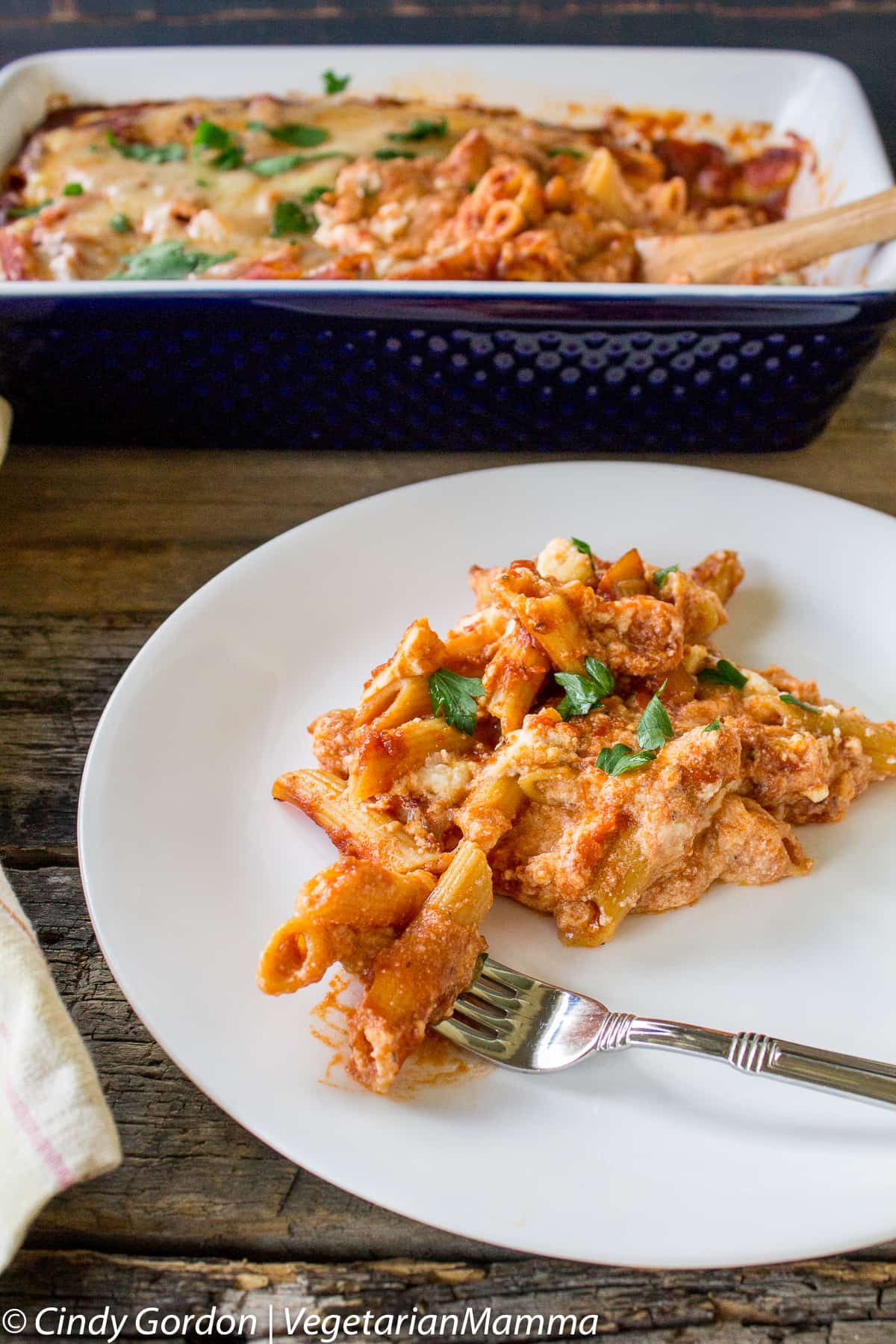 A white plate of deconstructed lasagna in front of a casserole dish with more lasagna