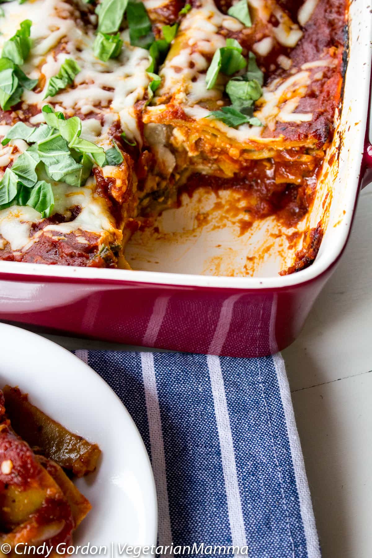 Spinach mushroom lasagna covered with chopped basil in a red and white casserole dish