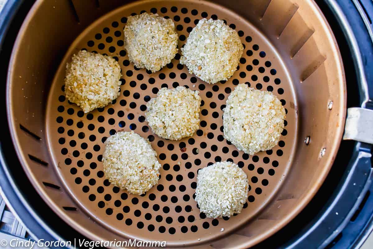 7 breaded rice balls in a round copper air fryer basket, viewed from above