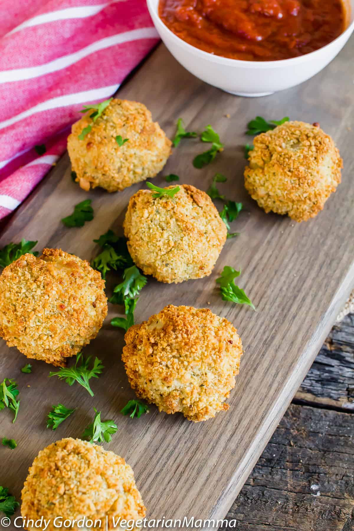 Air Fryer Risotto Balls on a wooden plank, next to a bowl of marinara sauce
