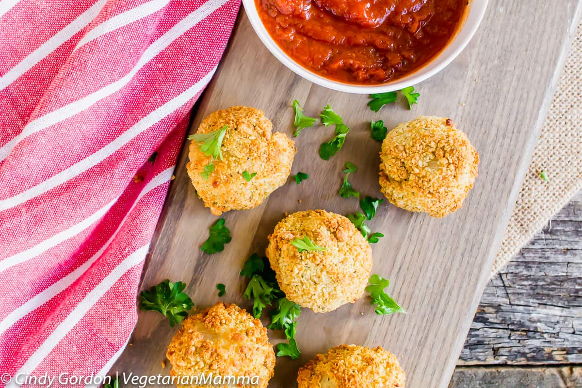 Air Fryer Risotto Balls on a wooden plank next to a bowl of marinara sauce
