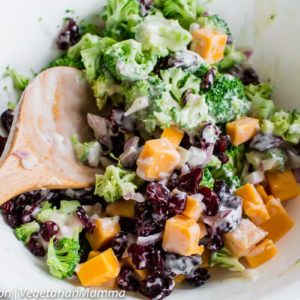 Spoon inside bowl of broccoli salad atop wooden pallet