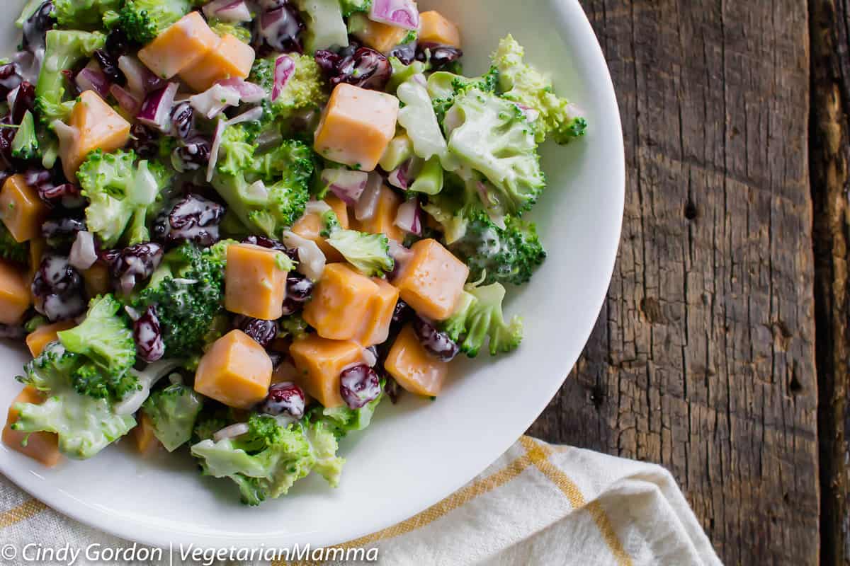 broccoli florets, cheddar cheese, and cranberries in a creamy dressing, all in a white bowl. 