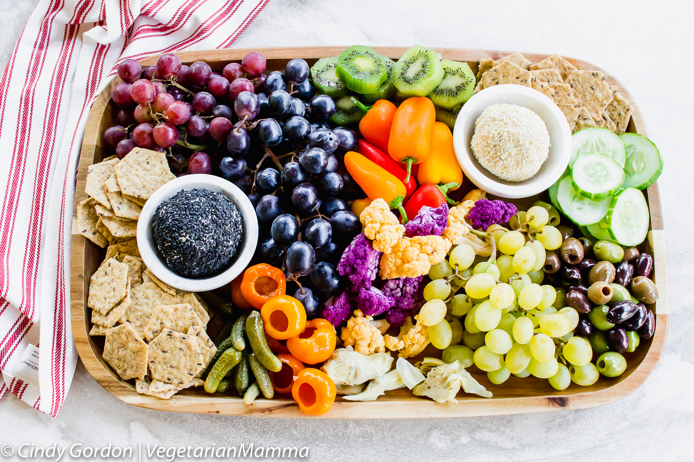 a wooden board filled with Vegetarian Charcuterie items like seed crackers, grapes, peppers, and cucumbers.