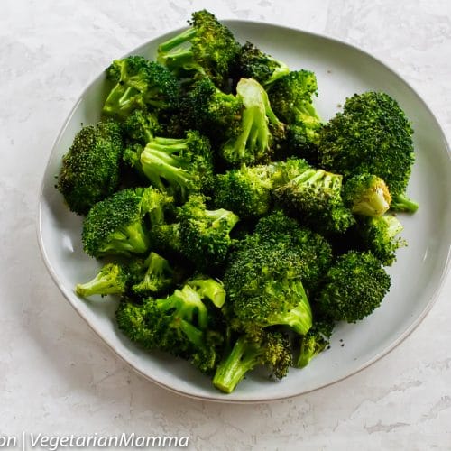 Top down view of broccoli on white plate atop white and gray table