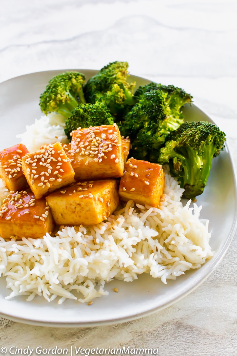 a plate of rice topped with saucy tofu and broccoli, topped with sesame seeds