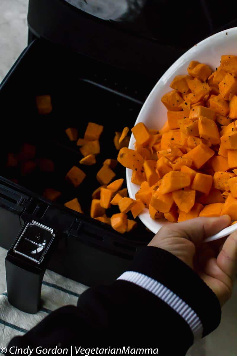 cubed sweet potatoes being tossed into air fryer basket