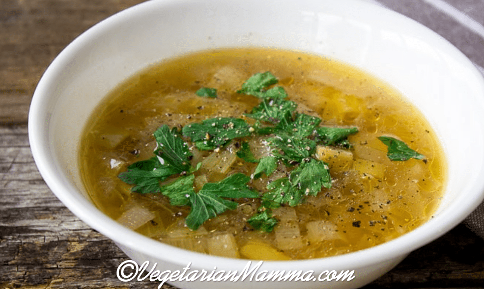 White bowl of potato leek soup on top of a board. 