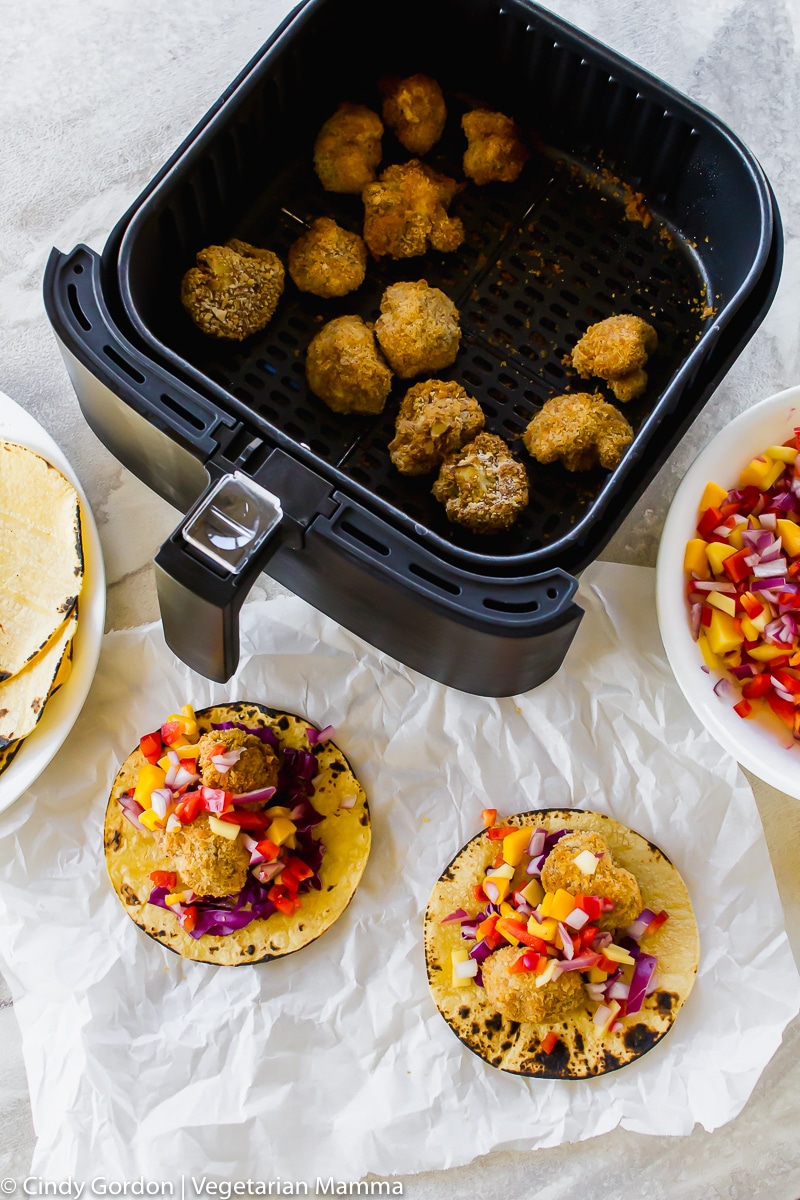 Over head shot of bread cauliflower bites in air fryer basket and corn tortilla tacos with cauliflower, purple cabbage and mango salsa