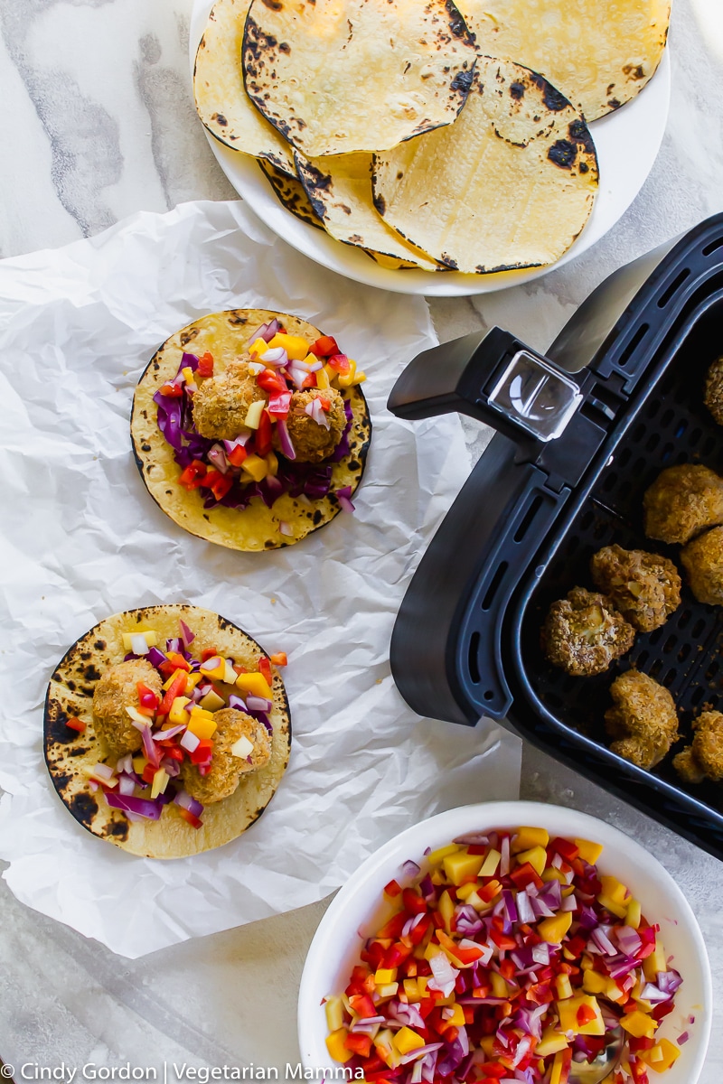 Overhead shot of cauliflower pieces cooked in air fryer basket and contructed tacos with mango slaw on top.
