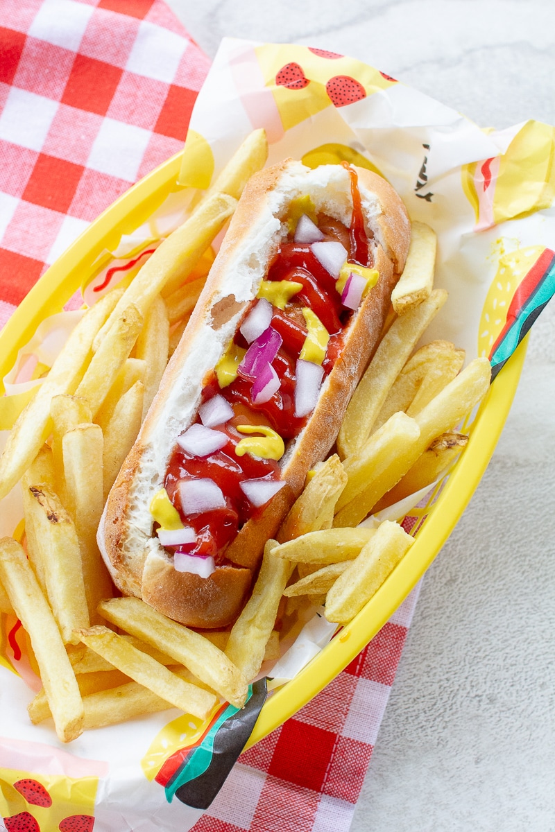 vertical picture of air fryer hot dogs in bun with fixings