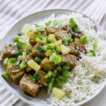 sweet and savory tofu with pineapple chunks on a plate of white rice.