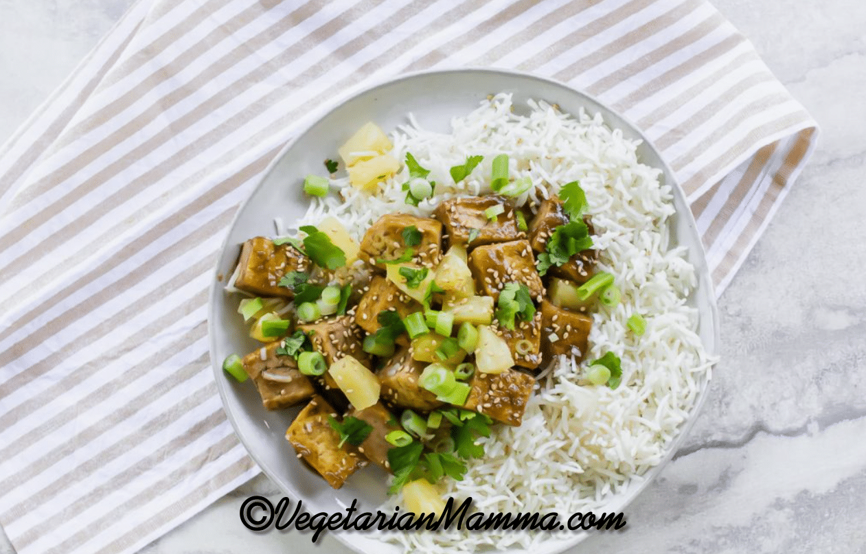 pineapple ginger tofu with pineapple chunks on a plate of white rice. 