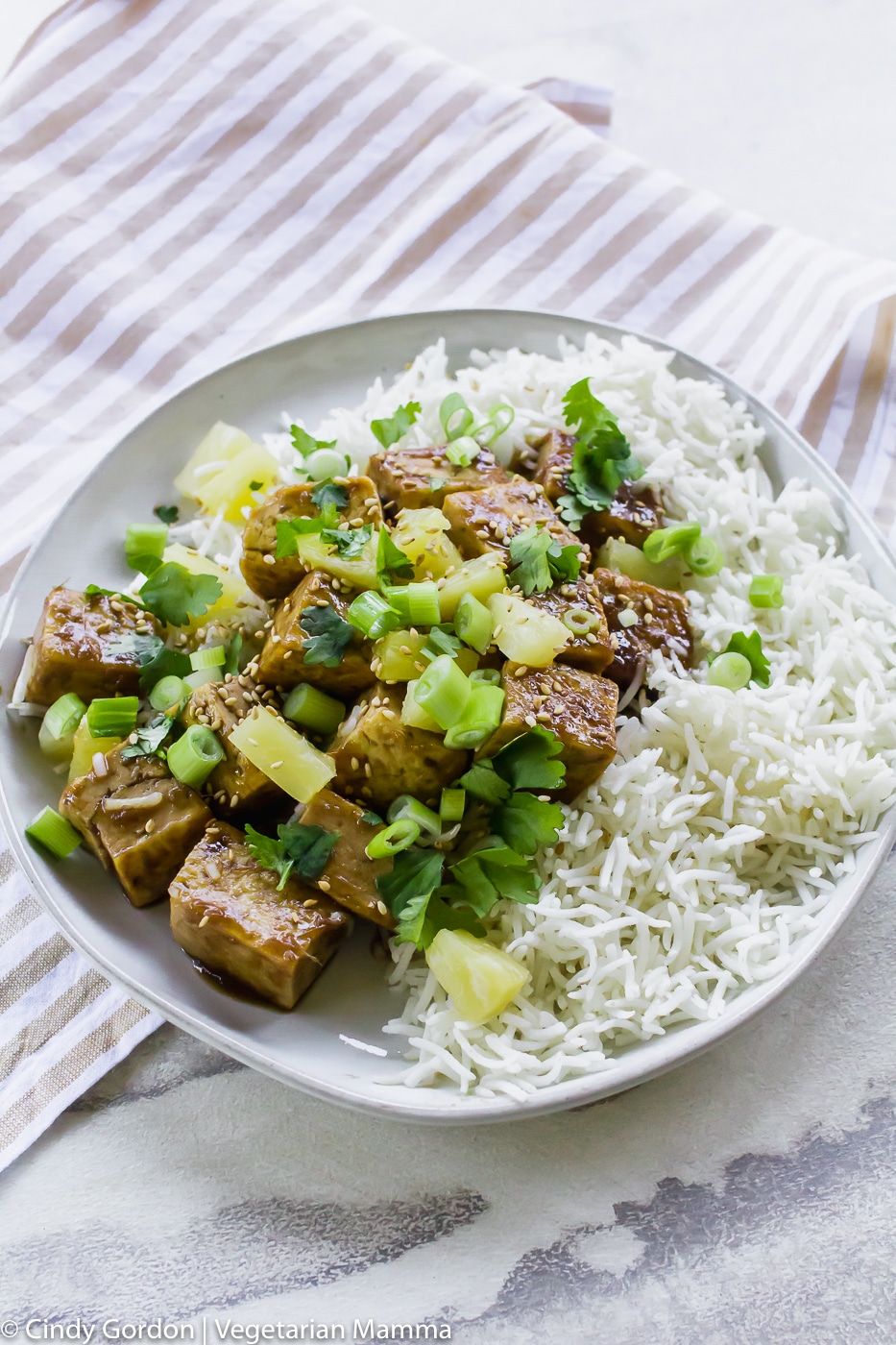 Pineapple Ginger Tofu with sauce and green onions on top on a white plate with a stripped napkin underneath