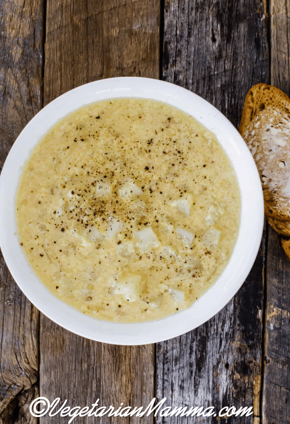A white bowl of soup with a slice of bread on a wooden table. 