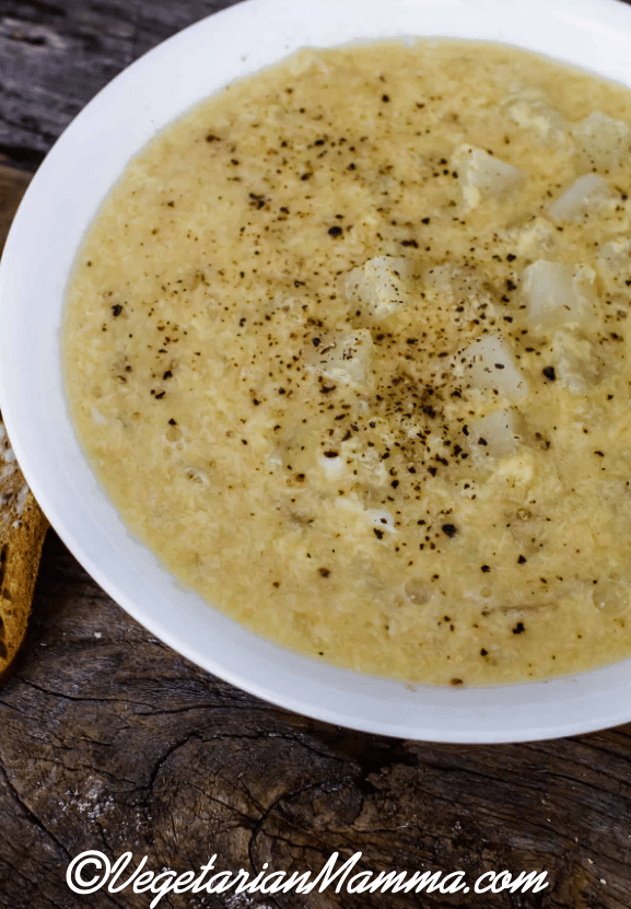 A white bowl of soup with a slice of bread on a wooden table. 