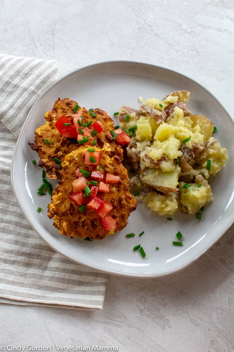 Air fryer zucchini fritters topped with diced tomato and on a white plate