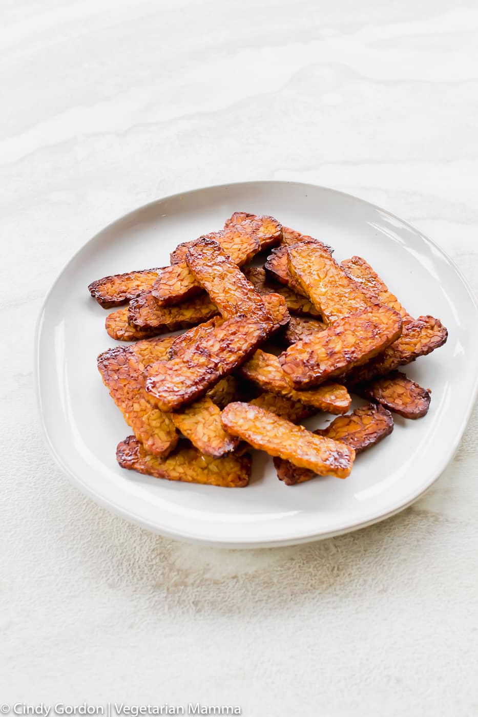 tall vertical picture of vegan bacon air fryer bacon on a white plate