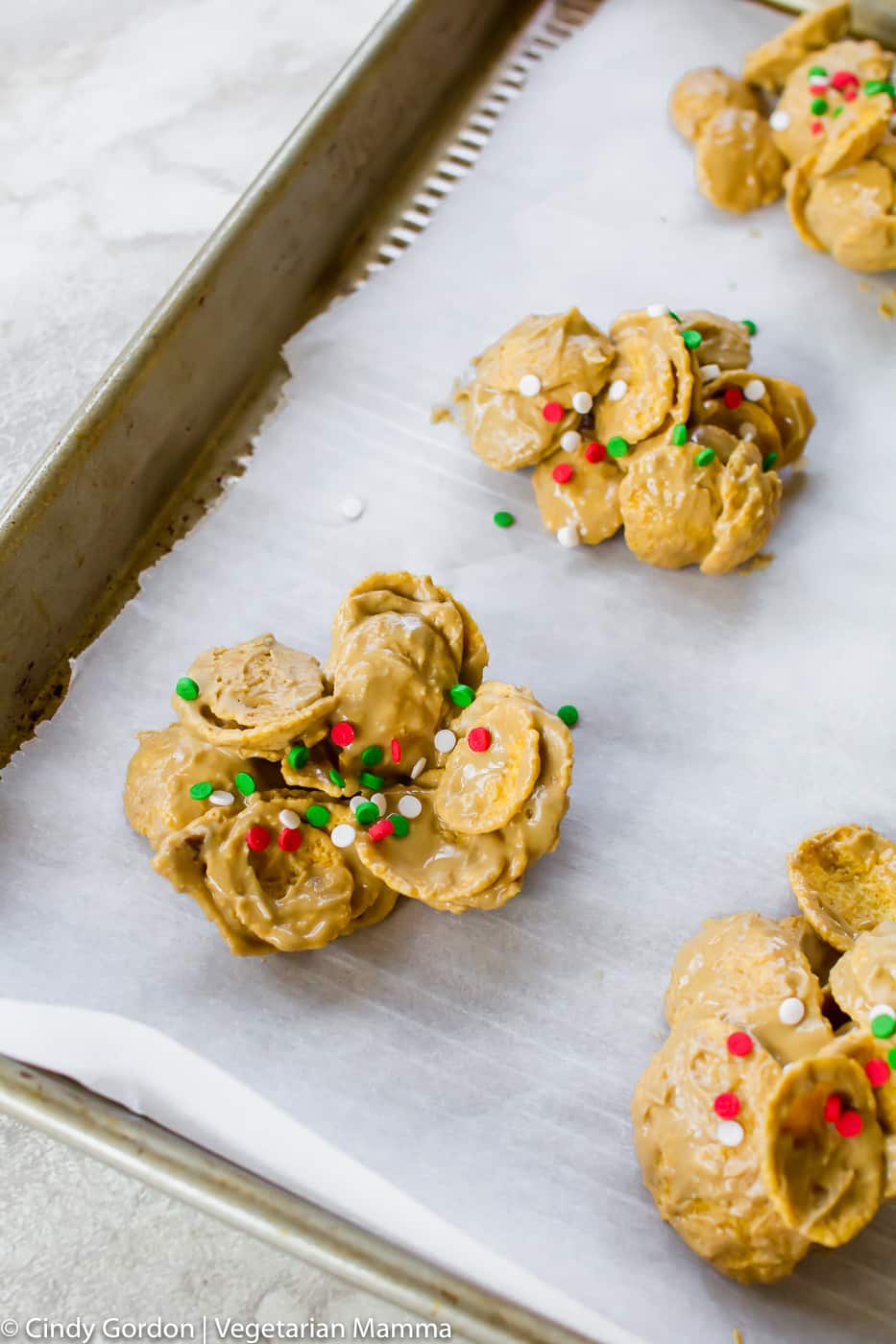Cornflake cookies with red, green and white sprinkles on top of parchment paper