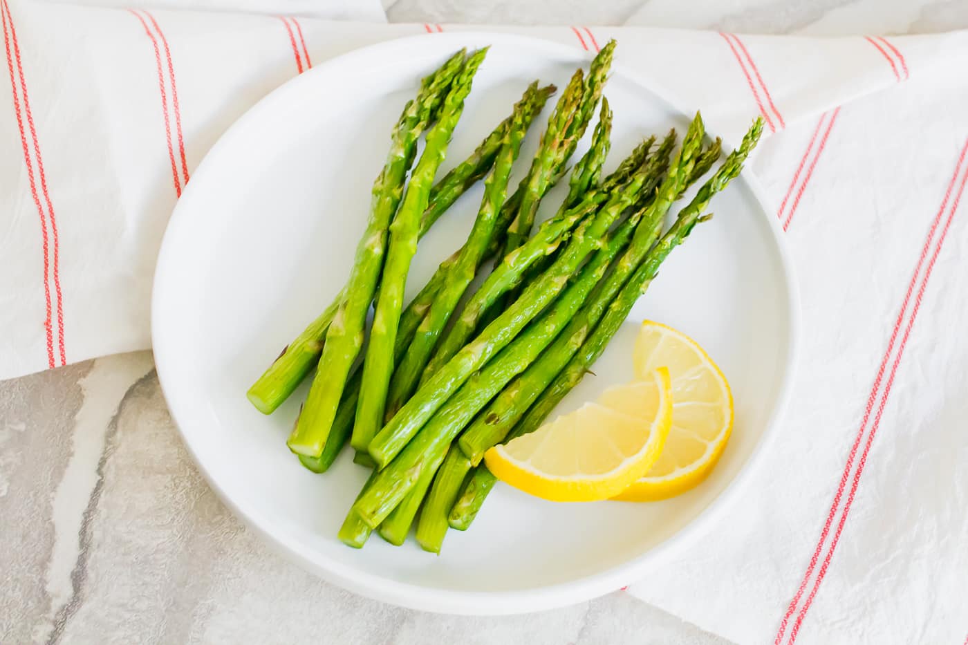 asparagus on a white plate with cut lemon on top of a white background