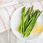 overhead shot of cooked air fryer asparagus on a white plate on top of a white and red striped napkin