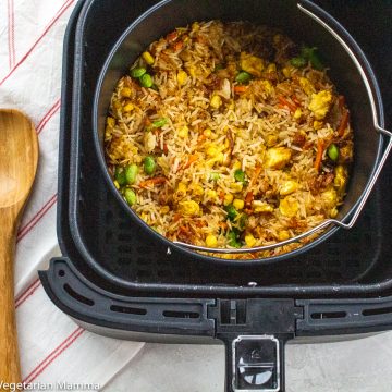 Multiple servings of fried rice in a black air fryer with a wooden spoon to the left