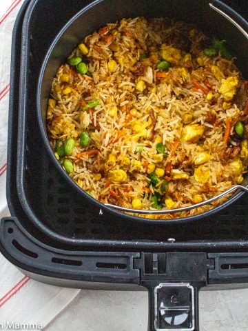 Multiple servings of fried rice in a black air fryer with a wooden spoon to the left
