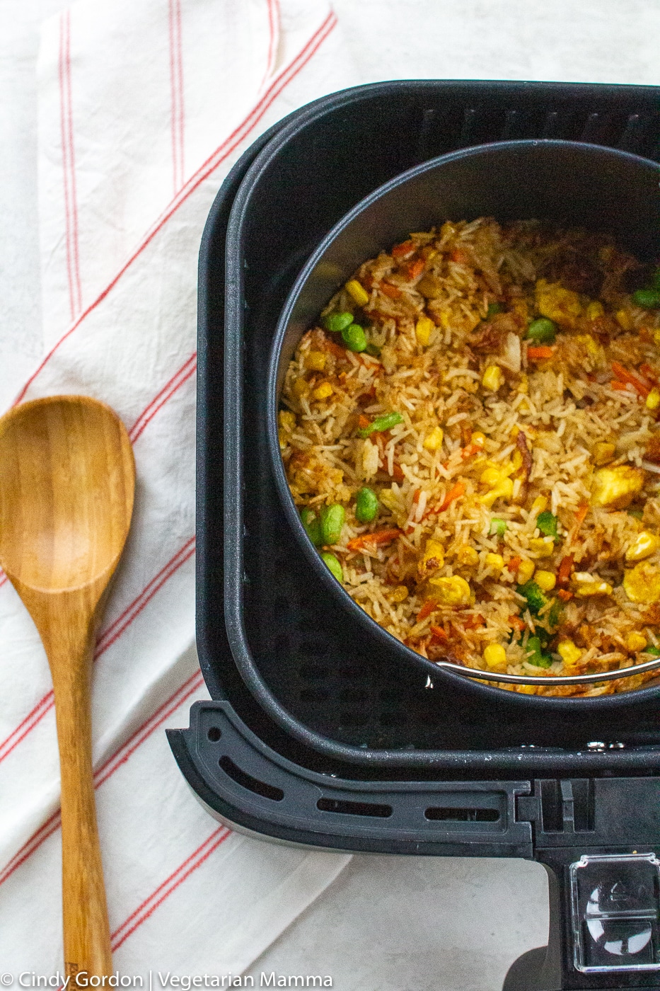 Air Fryer Fried Rice in air fryer basket with wooden spoon on the left