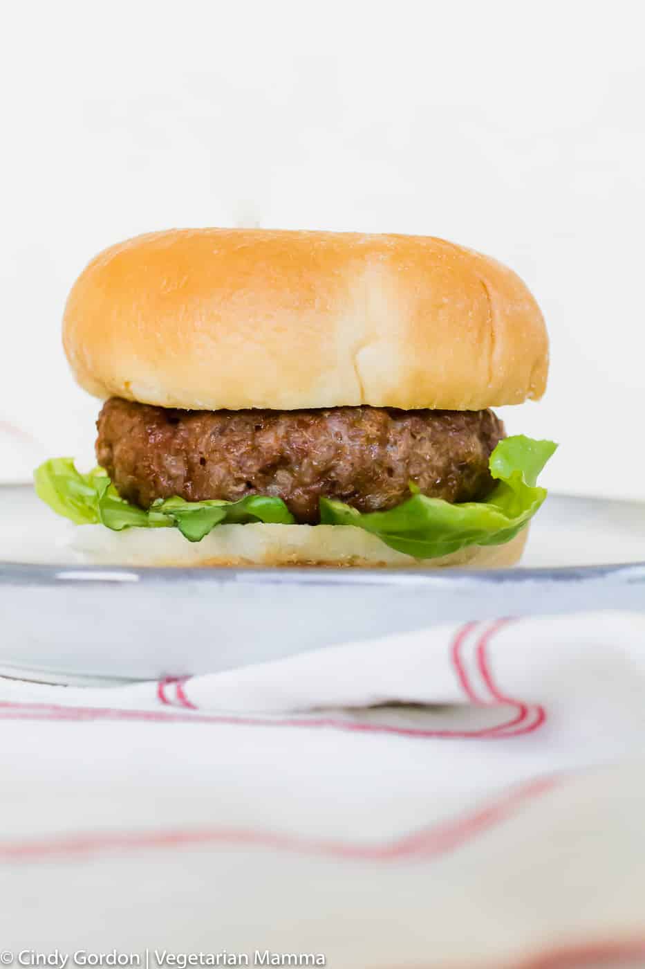 Air fryer burger on a bun with lettuce. ON a white plate and white back ground