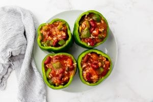 four green peppers stuffed with chunky red liquid on plate