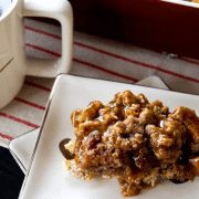 a serving of apple french toast casserole with caramel sauce on a square plate next to a cup of coffee