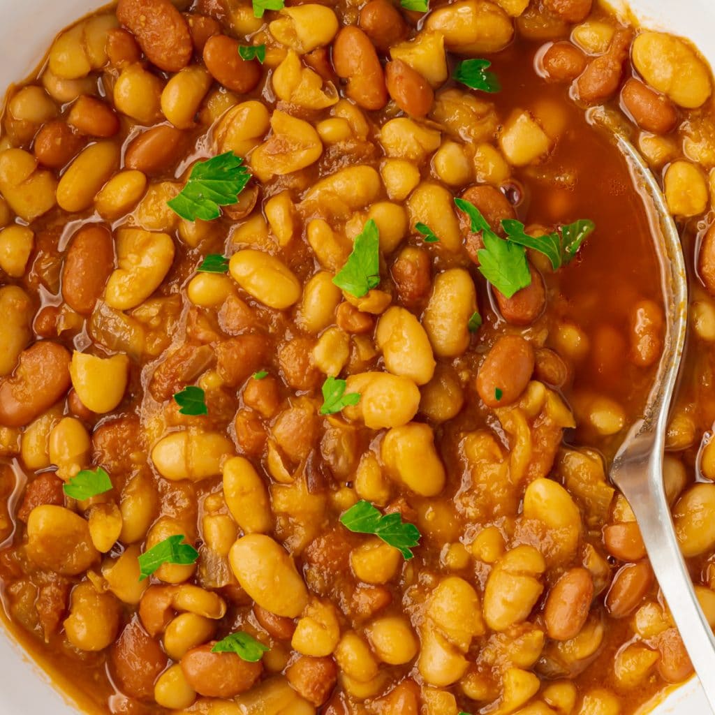 brown and golden beans in red liquid with green herbs on top