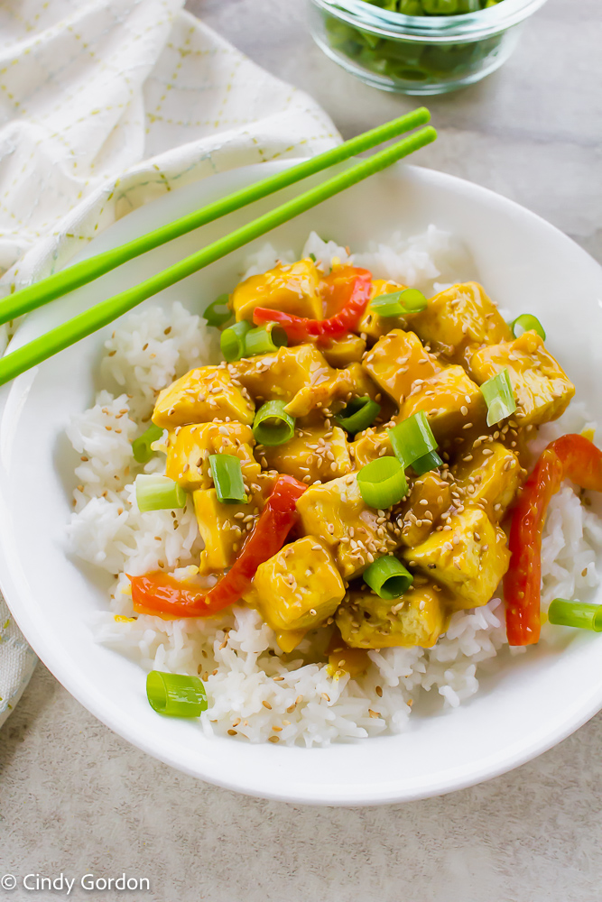 orange tofu in a white bowl on a white background tabletop with green chopsticks