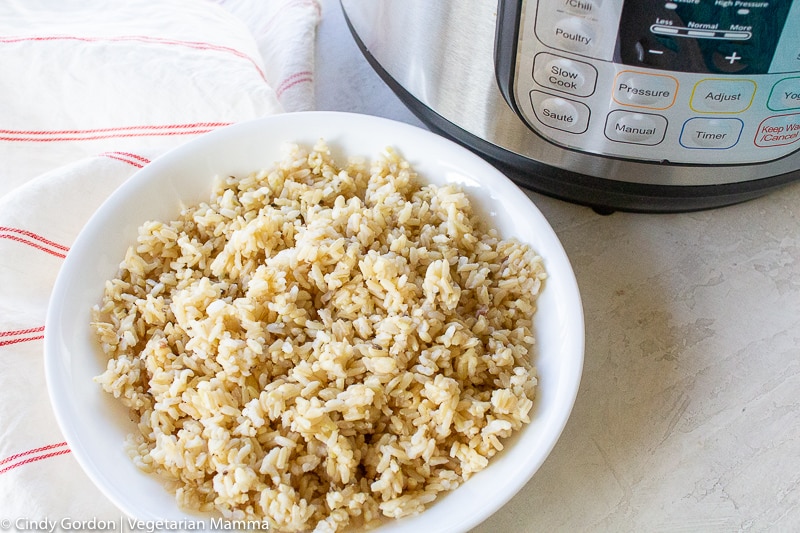 a white bowl filled with brown rice beside an instant pot