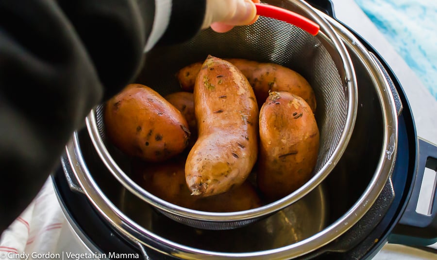 a hand placing a steamer basket filled with sweet potatoes into a pressure cooker
