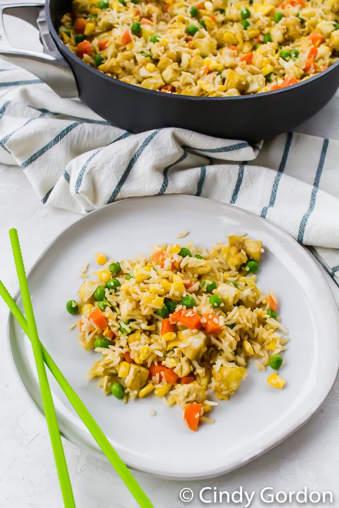 fried rice with carrots, peas, corn, and tofu on a white plate with chopsticks