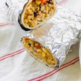 two burritos with rice and vegetables wrapped in foil