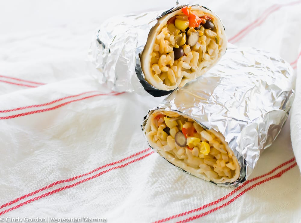 two burritos filled with rice and vegetables and wrapped in foil