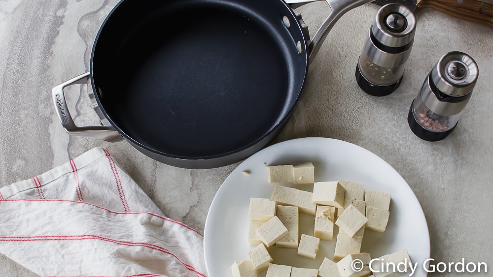 overhead picture of black skillet, cubed tofu, white napkin with red stripes and salt and pepper shakers