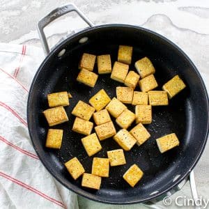 black skillet with golden crisp pan fried tofu with some oil