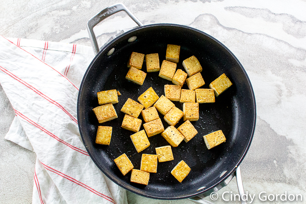 black skillet with golden crisp pan fried tofu with some oil