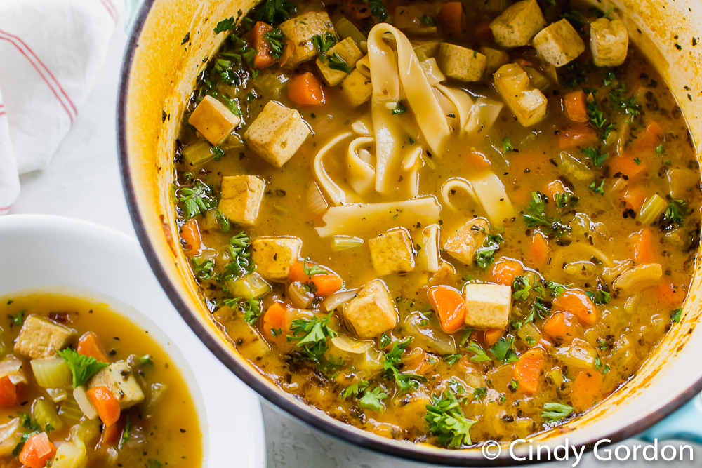 a pot of noodle soup with diced vegetables and tofu