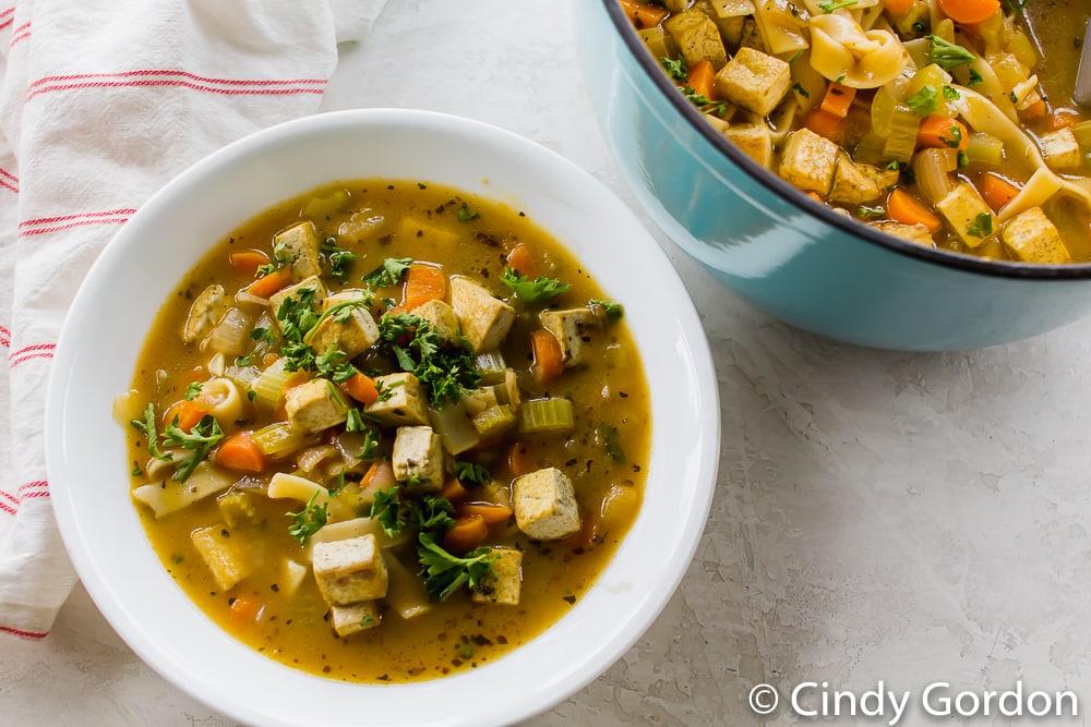 a white bowl full of tofu noodle soup beside a blue pot of the same soup