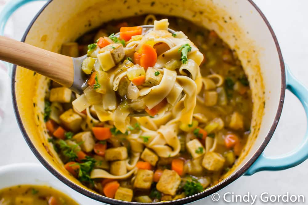 a ladle scooping a serving of soup with noodles and vegetables out of a pot of soup