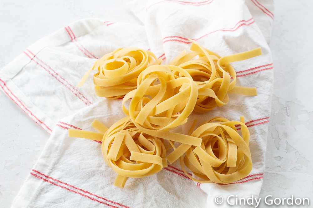 bundles of uncooked flat pasta on a white towel with thin red stripes